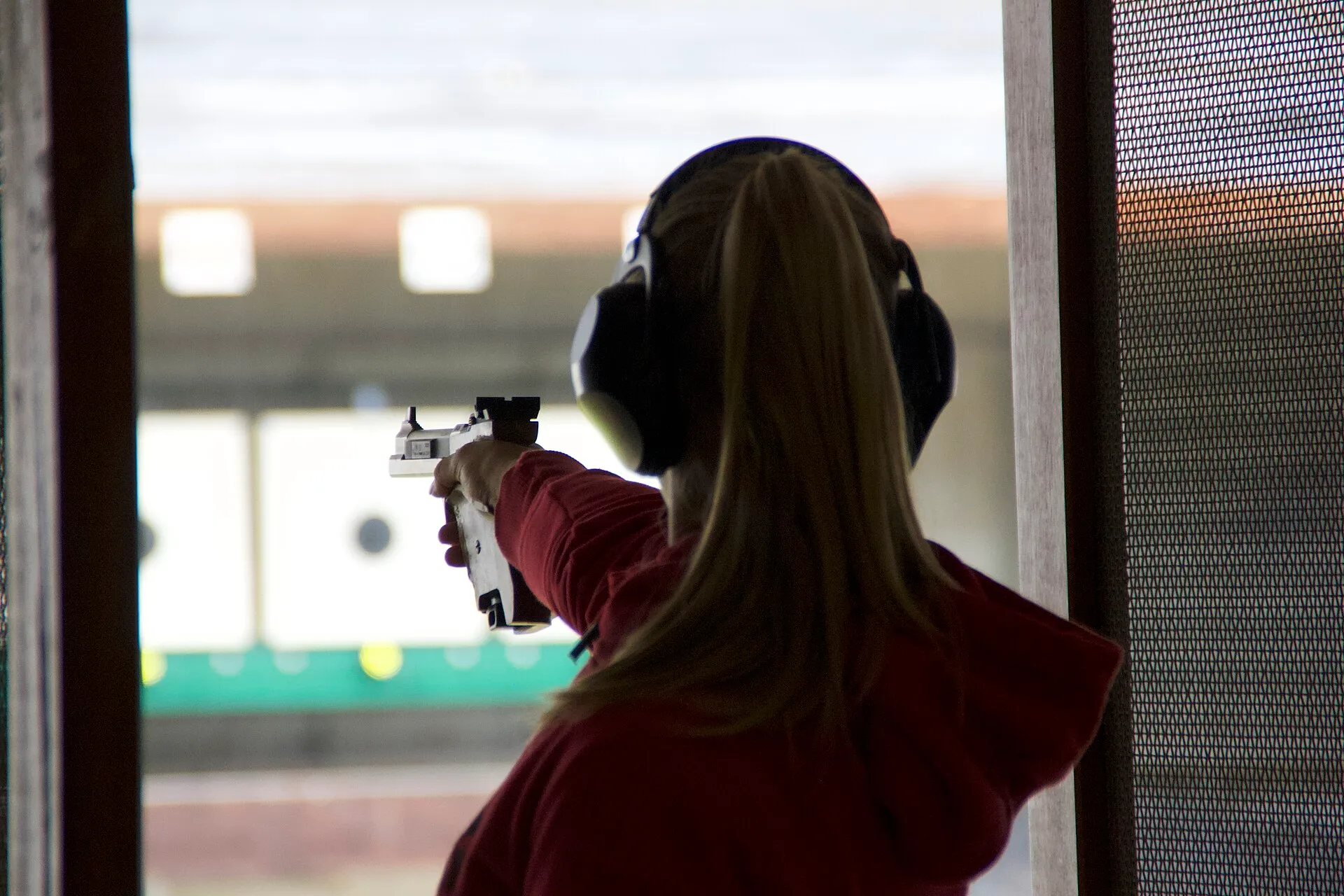 Sportschützin mit Gehörschutz von hinten, den Blick auf die Scheiben gerichtet