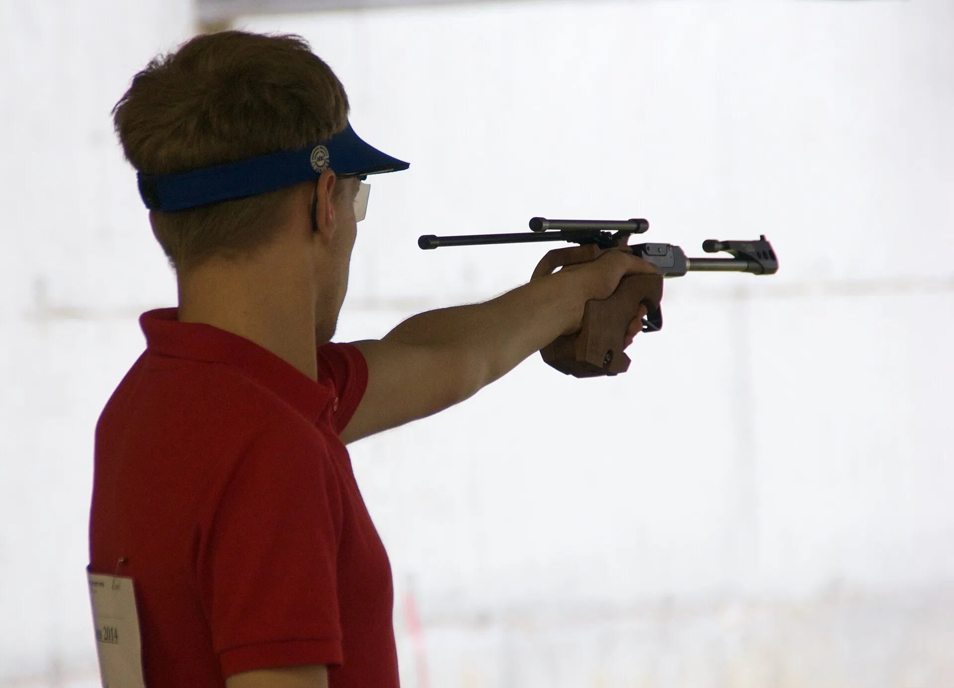 Sportschütze mit Schirmmütze im Profil, die Sportpistole in Richtung der Scheibe